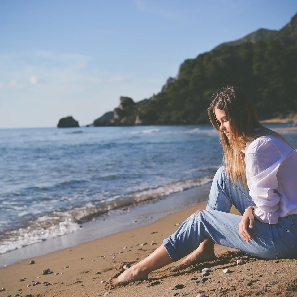 A young woman sitting calmly on a bright sunlit beach shore in clear daylight