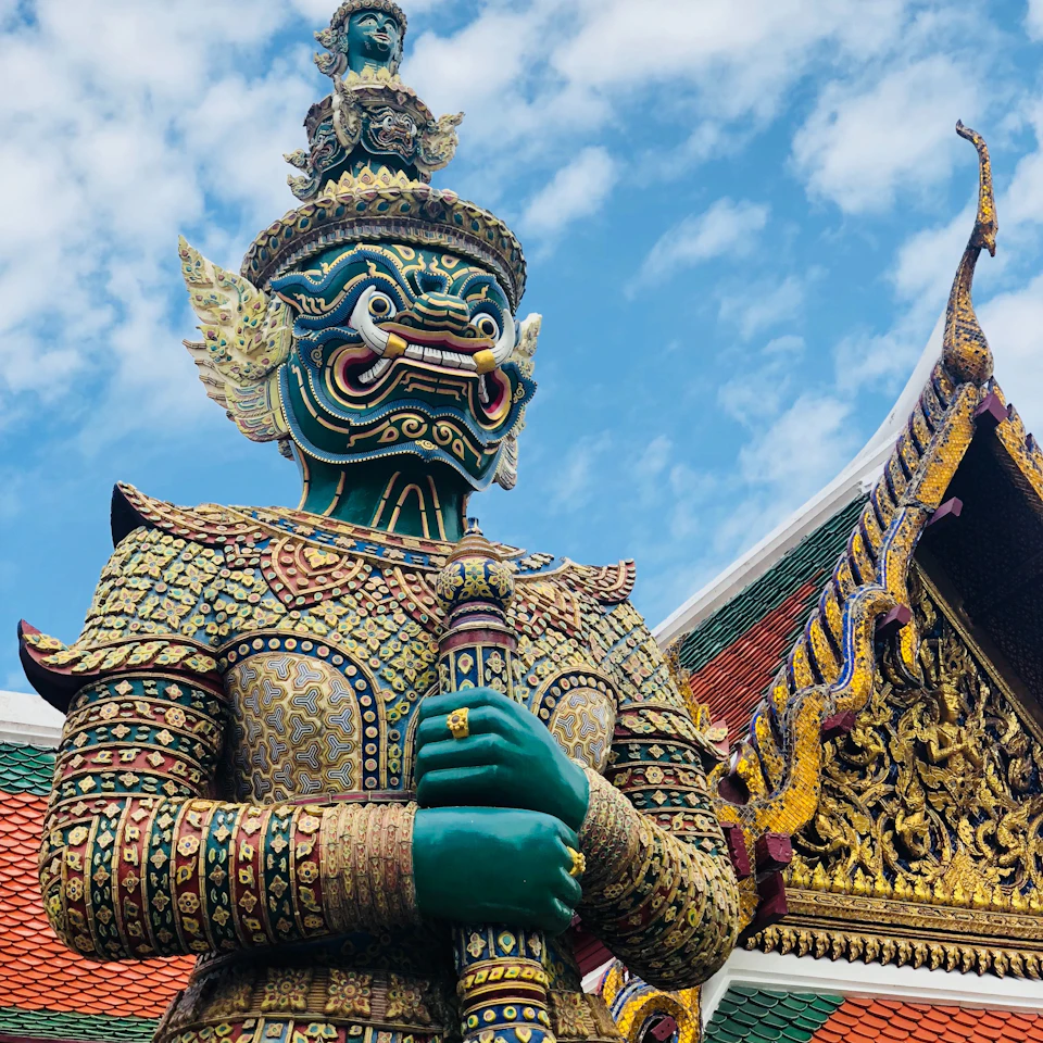 Ornate gold and green temple guardian at Bangkok Grand Palace against a vivid blue sky