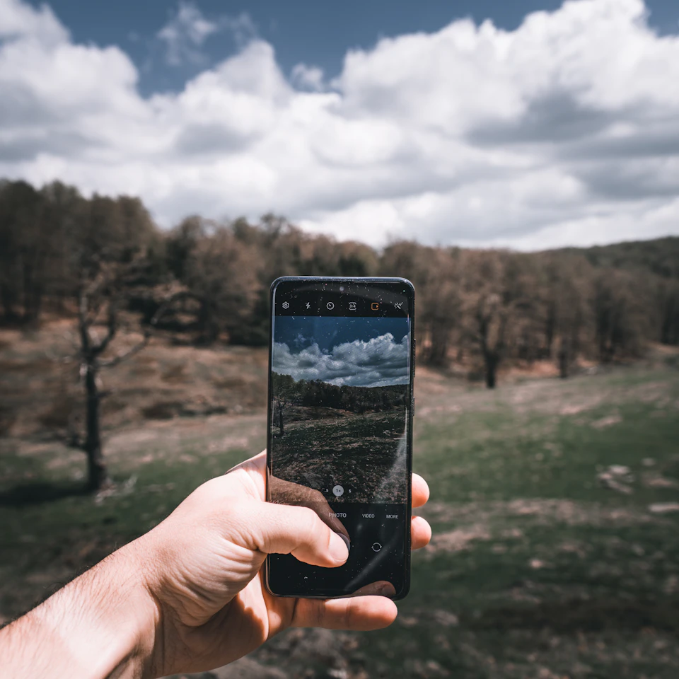 A young person filming a sunny landscape on a phone, a bright fun travel-content vibe