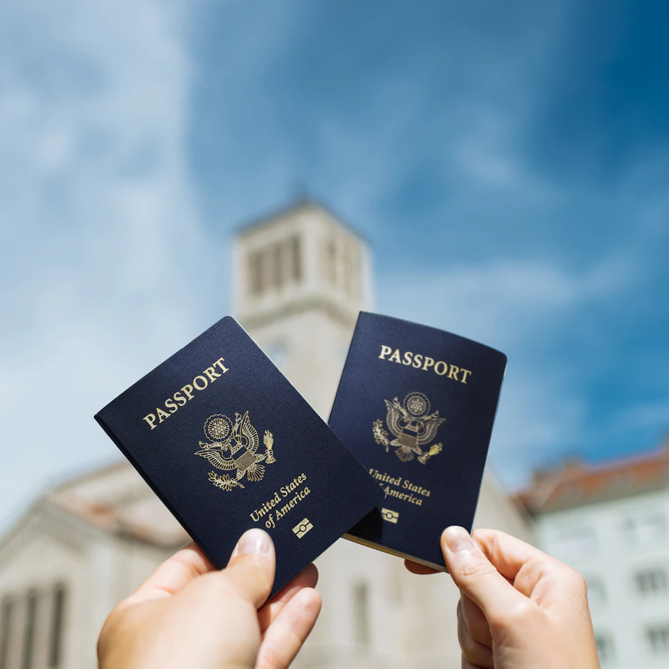 Two cheerful travelers holding up their passports in bright daylight