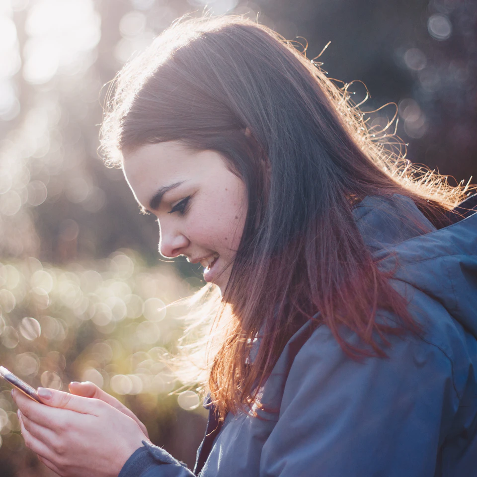 A smiling young woman scrolling her phone happily in bright natural daylight
