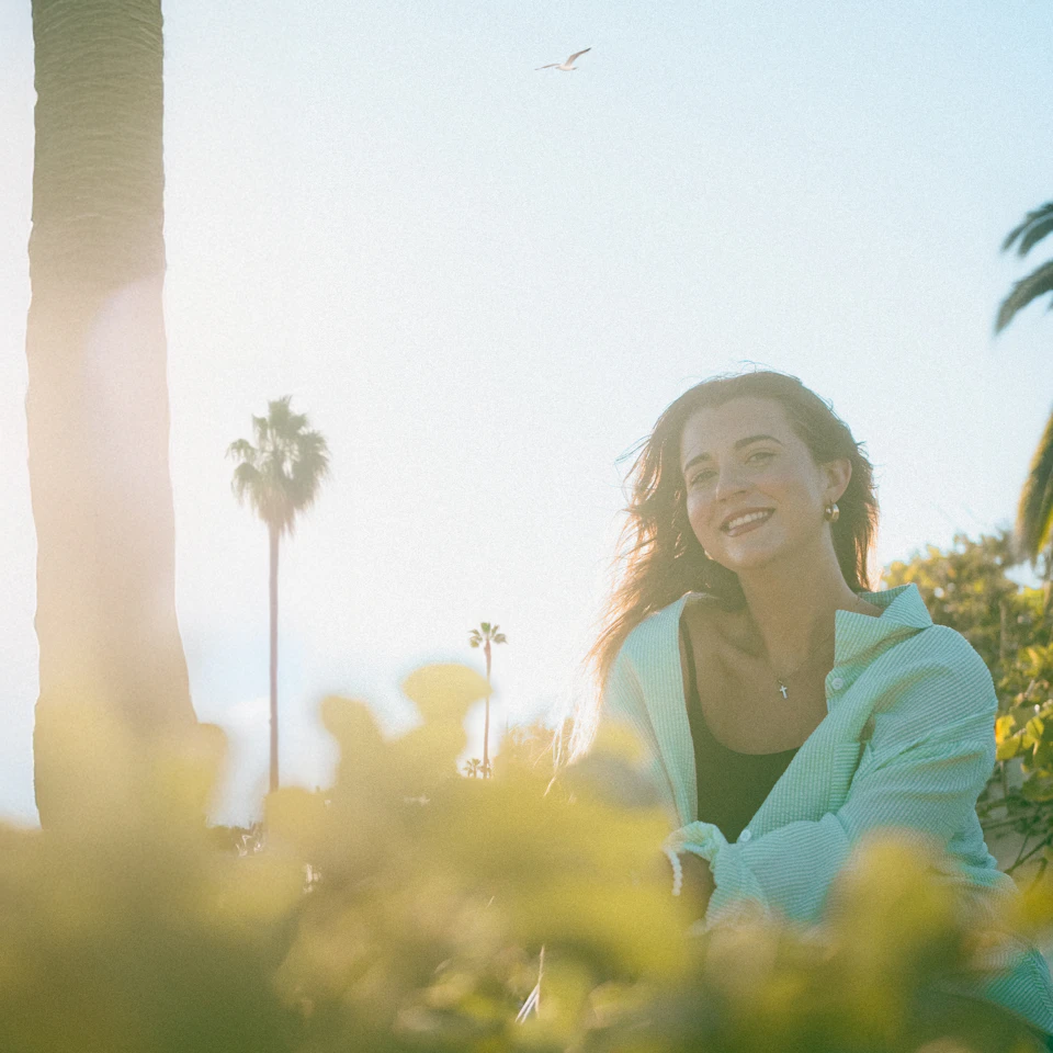 Smiling young woman outdoors in bright sunlight with palm trees, looking happy and free