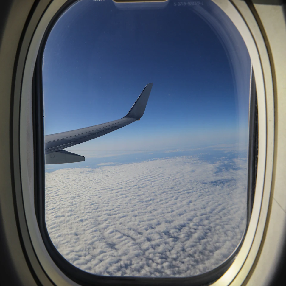 A bright airplane window looking out over clouds and blue sky in clear daylight