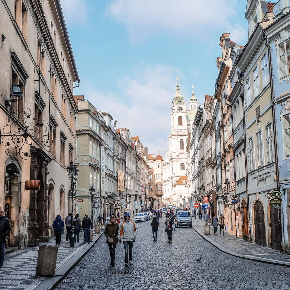 A sunny European street with people strolling between bright buildings on a clear day